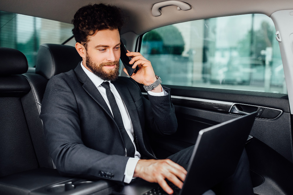 Business professional working on a laptop while talking on the phone in the back seat of a luxury car with a private chauffeur in Dubai.