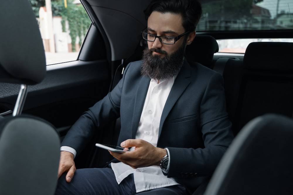 Business professional using a smartphone while traveling comfortably in a chauffeur-driven car, showcasing Weekly basis chauffeur service in UAE.
